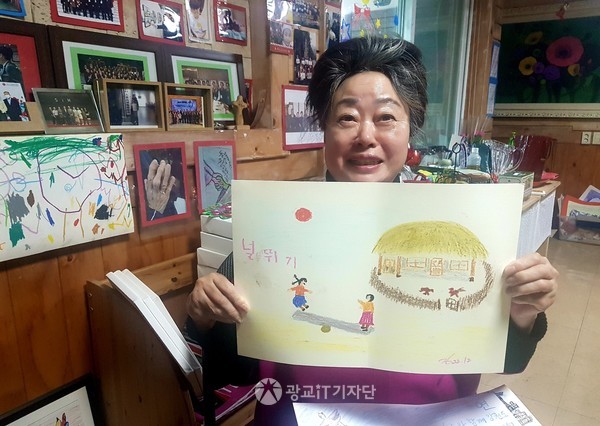 ▲신현옥 회장이 신년을 앞두고 널뛰기 그림을 그린 어르신의 작품을 선보이고 있다.